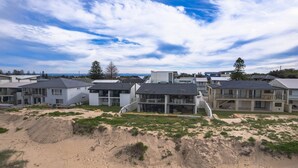 A coastal residential area with modern houses, sandy terrain, and a clear sky. - Time and Tides - Beachfront, Stunning Ocean Views. (THE ENTRANCE NORTH)