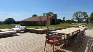 A wooden deck with a table and chairs, a lounge area, and a stone building in the background. - Beautiful villa with indoor pool (Sainte-Cécile)