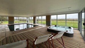 A spacious indoor pool area with a hot tub, wooden deck, and large windows offering a view of the outdoors. - Beautiful villa with indoor pool (Sainte-Cécile)
