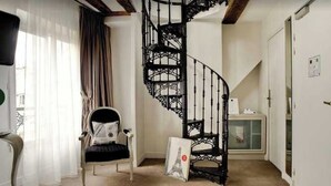Una habitación con escalera de caracol, una silla, un marco de foto y una puerta.