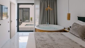 Une chambre moderne dotée d’un grand lit, d’une baignoire et offrant une vue sur une piscine et un espace de détente extérieur.