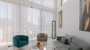 Un salon moderne avec un fauteuil turquoise, un fauteuil beige et un canapé gris. On y trouve une table basse en bois, sur laquelle sont posés un livre et un verre.