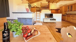 Uma cozinha acolhedora com vigas de madeira, uma sala de jantar com mesa posta para refeição, e uma escada que leva a um andar superior.