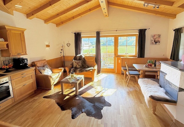 A spacious living area with a wooden ceiling, a kitchen with a stove, a dining table, and a sofa.