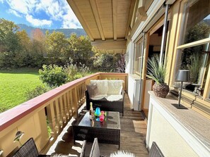 A covered balcony with wicker furniture, a table with bottles, and a potted plant.