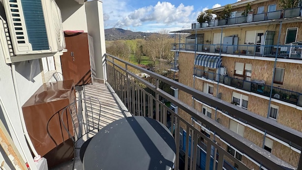 Un balcon donnant sur un immeuble à plusieurs étages, avec une antenne parabolique et un meuble en bois.