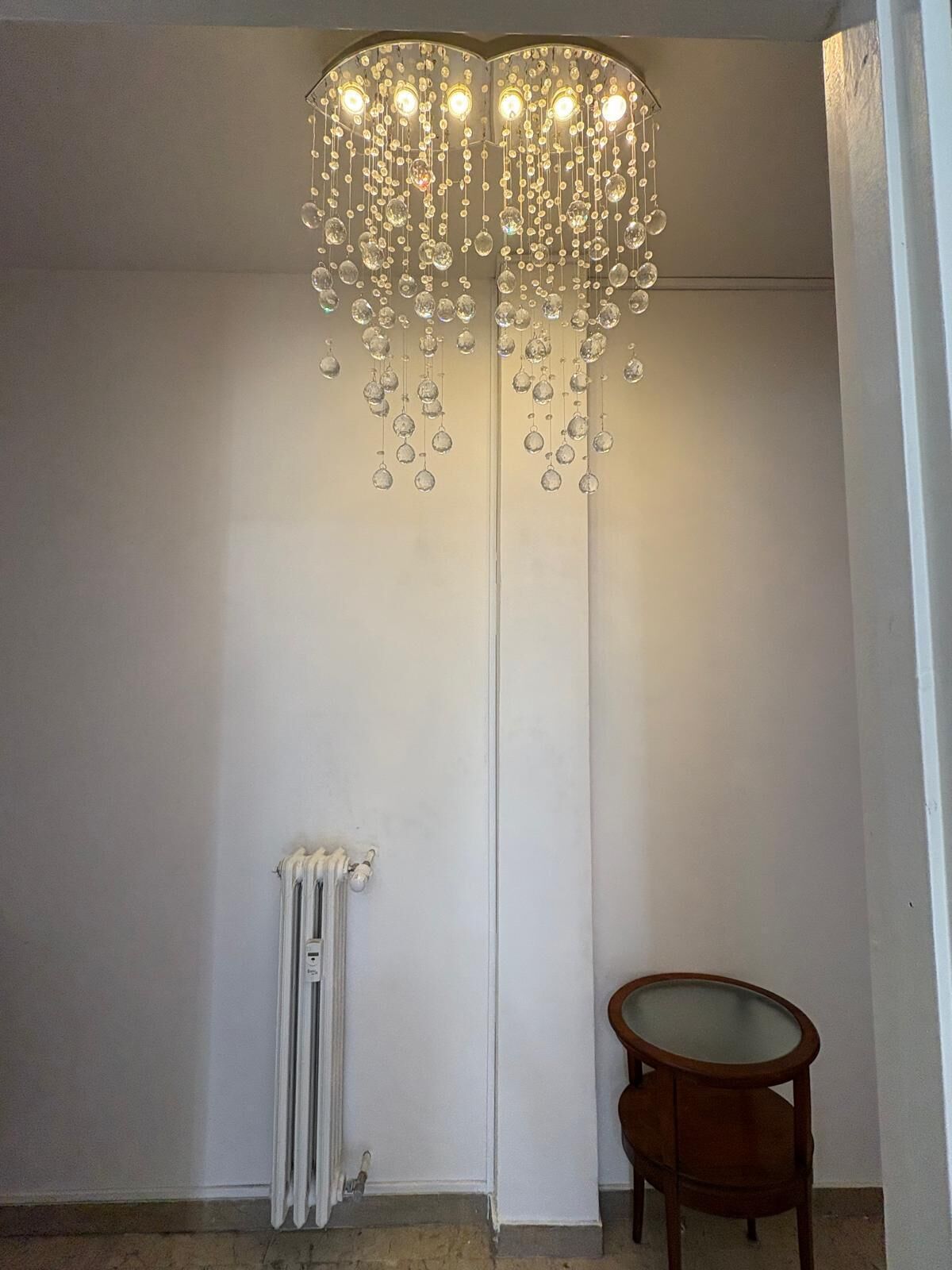 A room with a white radiator, a wooden chair, and a hanging chandelier.