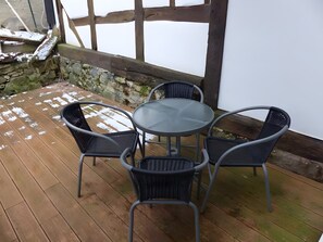 Une terrasse en bois avec une table en verre et quatre chaises.