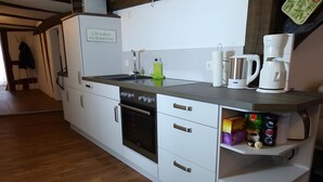 A modern kitchen with white cabinetry, a built-in oven, a coffee maker, and a shelf with various items. - Apartment 'Homberger Altstadt' with private terrace and Wi-Fi (Homberg (Efze))