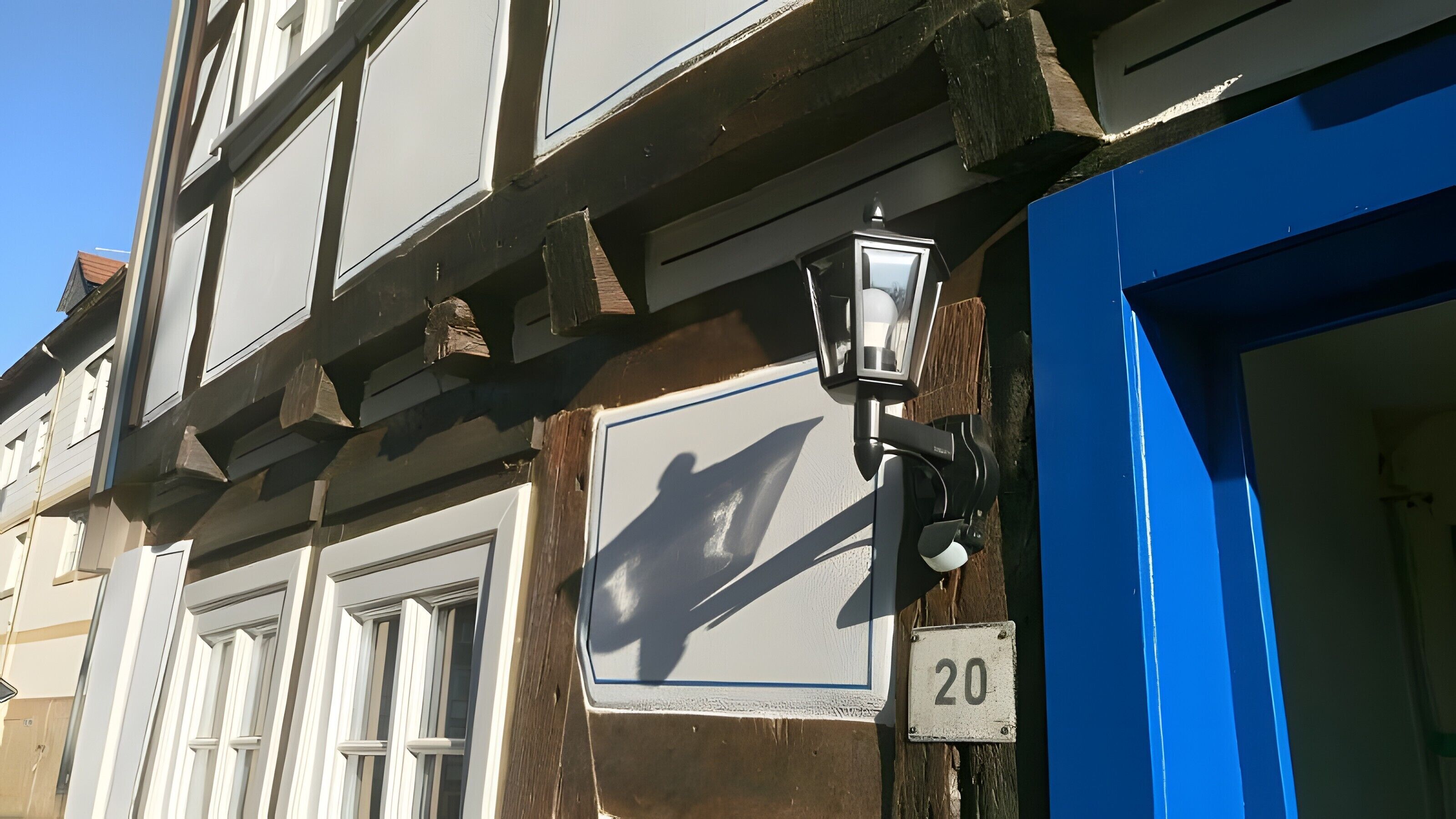 Eine Gebäudefassade mit blauer Tür, der Hausnummer 20 und einem traditionellen Fenster mit Fensterläden.