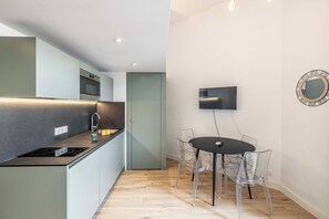 A modern kitchen with a built-in stove, a dining area with a table and chairs, a flat-screen TV mounted on the wall, and a mirror.