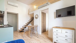 Ein kompakter Wohnbereich mit Küchenzeile, Essbereich, Treppe und einem an der Wand befestigten Fernseher.