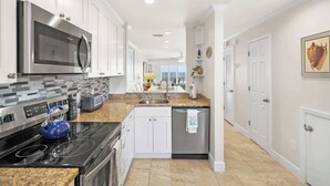 A modern kitchen with white cabinets, stainless steel appliances, and a granite countertop. - Oceanfront, Pool, Tennis, BBQ, Patio, Free Parking (St. Augustine)