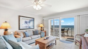 A living room with a sofa, coffee table, and a view of the ocean through a sliding glass door. - Oceanfront, Pool, Tennis, BBQ, Patio, Free Parking (St. Augustine)
