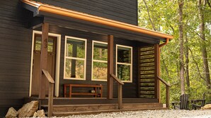 Una cabaña de madera con porche, ventanas amplias y un banco.