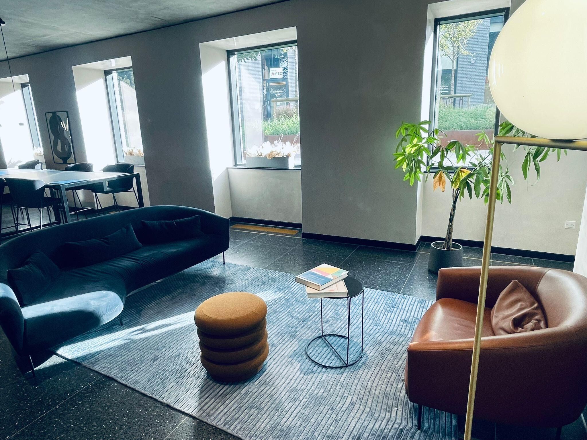 Un intérieur moderne avec un canapé noir, un pouf marron, un fauteuil en cuir et une petite table sur laquelle repose un livre.