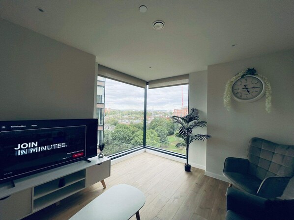 Ein modernes Wohnzimmer mit großem Fenster, einem Flachbildfernseher, einer Pflanze und einer Wanduhr.
