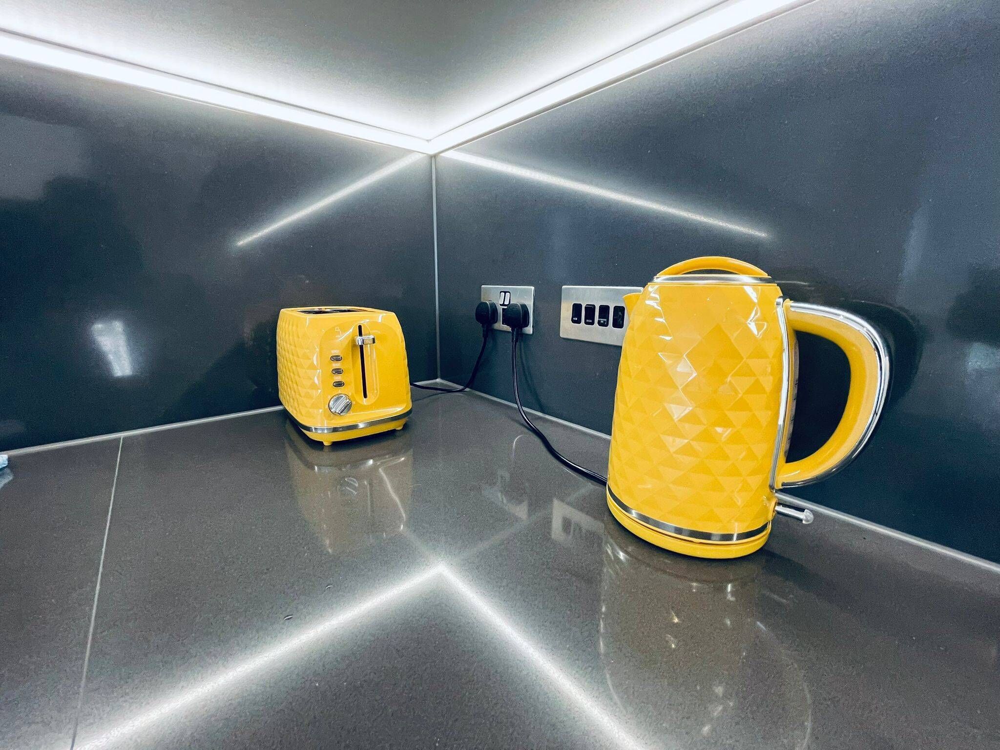 A modern kitchen with a yellow toaster and kettle on a sleek countertop, connected to a power outlet.