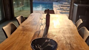 A wooden dining table with wine glasses and a bottle, overlooking a swimming pool. - Bellevia Stone Pool Villa (Nea Styra)