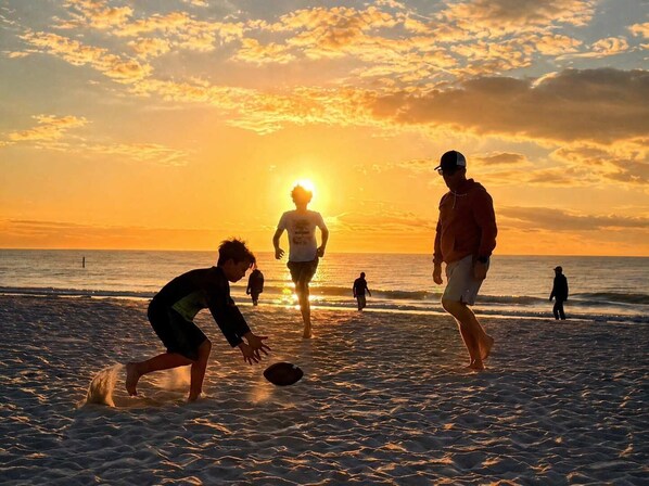 A beach scene with people playing frisbee during sunset.