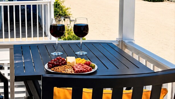 Una mesa con dos copas de vino y un plato de aperitivos en un balcón con vistas a la playa.