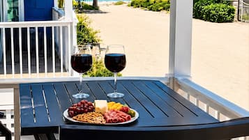 A table with two wine glasses and a plate of snacks on a balcony overlooking a beach.