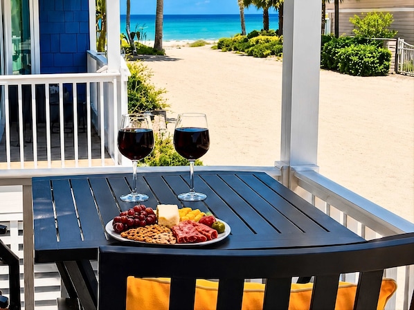 A table with two wine glasses and a plate of snacks on a balcony overlooking a beach.
