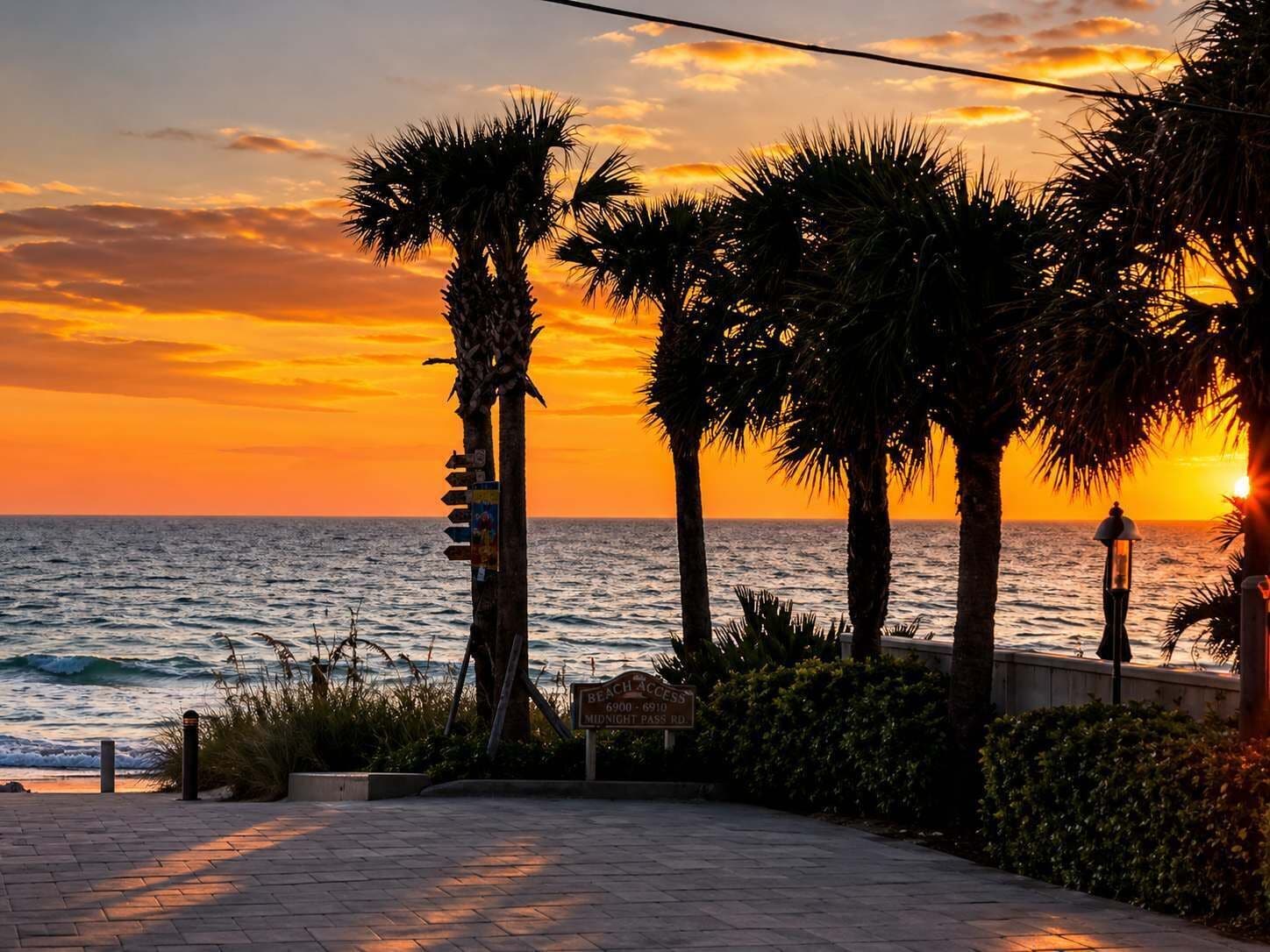 A sunset view with palm trees and a sign indicating 'Beach Access' and 'Midnight Pass Rd.'