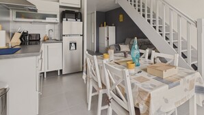 A compact kitchen with modern appliances, a dining area with a table set for four, and a staircase leading to an upper level.