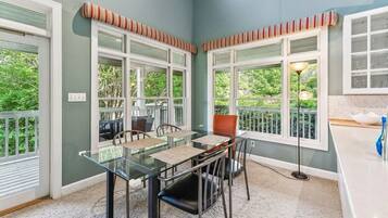 Un comedor con una mesa y sillas de vidrio, cortinas de ventana a rayas y vistas de la vegetación exterior.