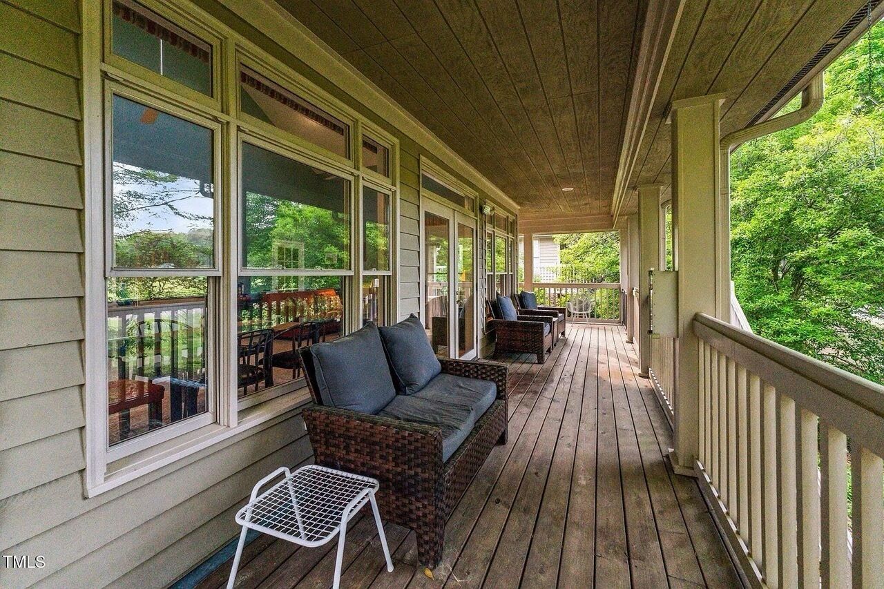 A covered porch with wicker furniture, large windows, and a view of greenery.