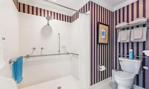 Un baño con bañera, ducha, inodoro y paredes a rayas.