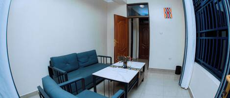 A compact living space with a sofa set, a small table, and a window with a metal grill.
