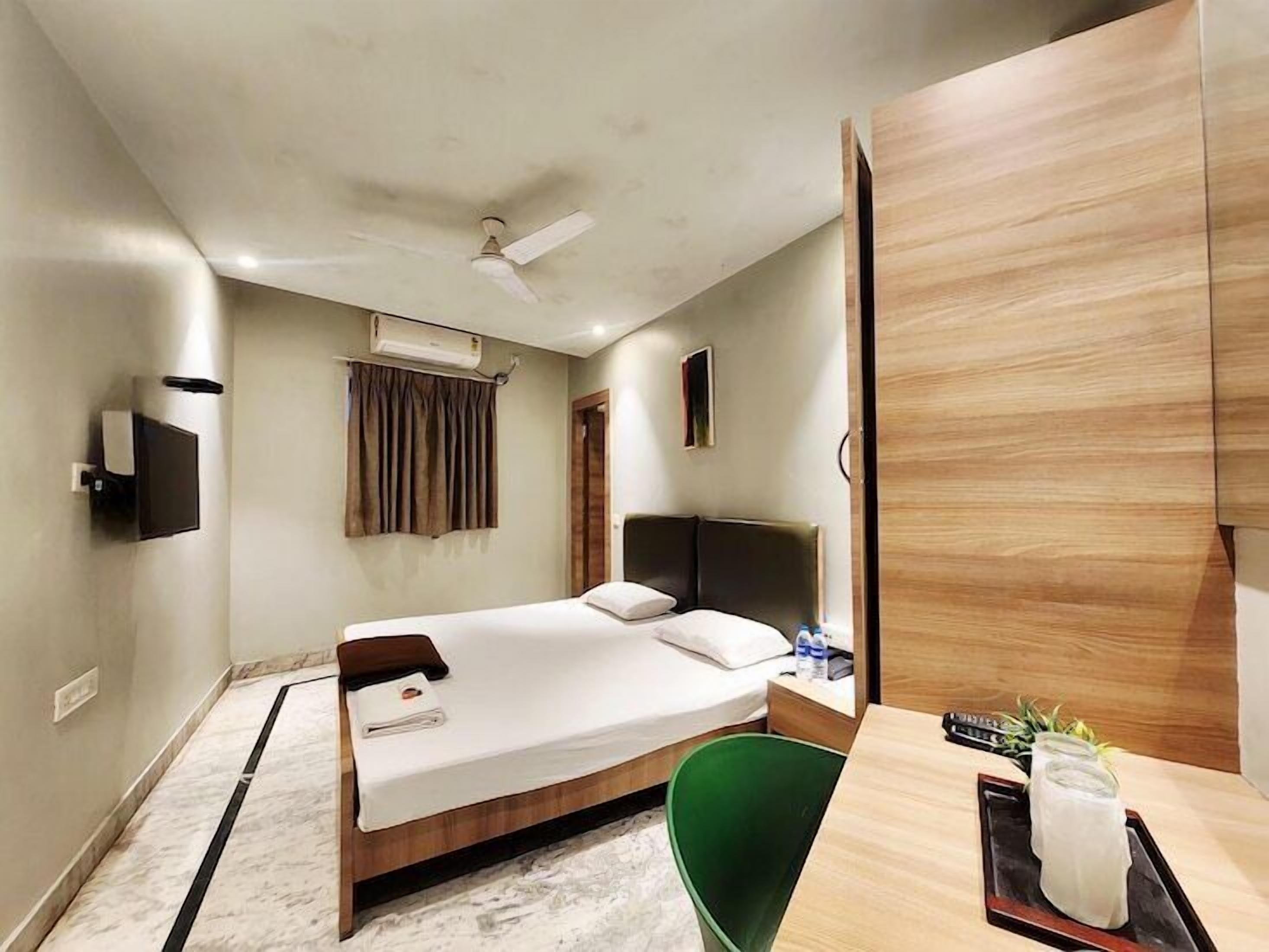 A hotel room with a bed, a desk, a chair, a TV, and a ceiling fan.