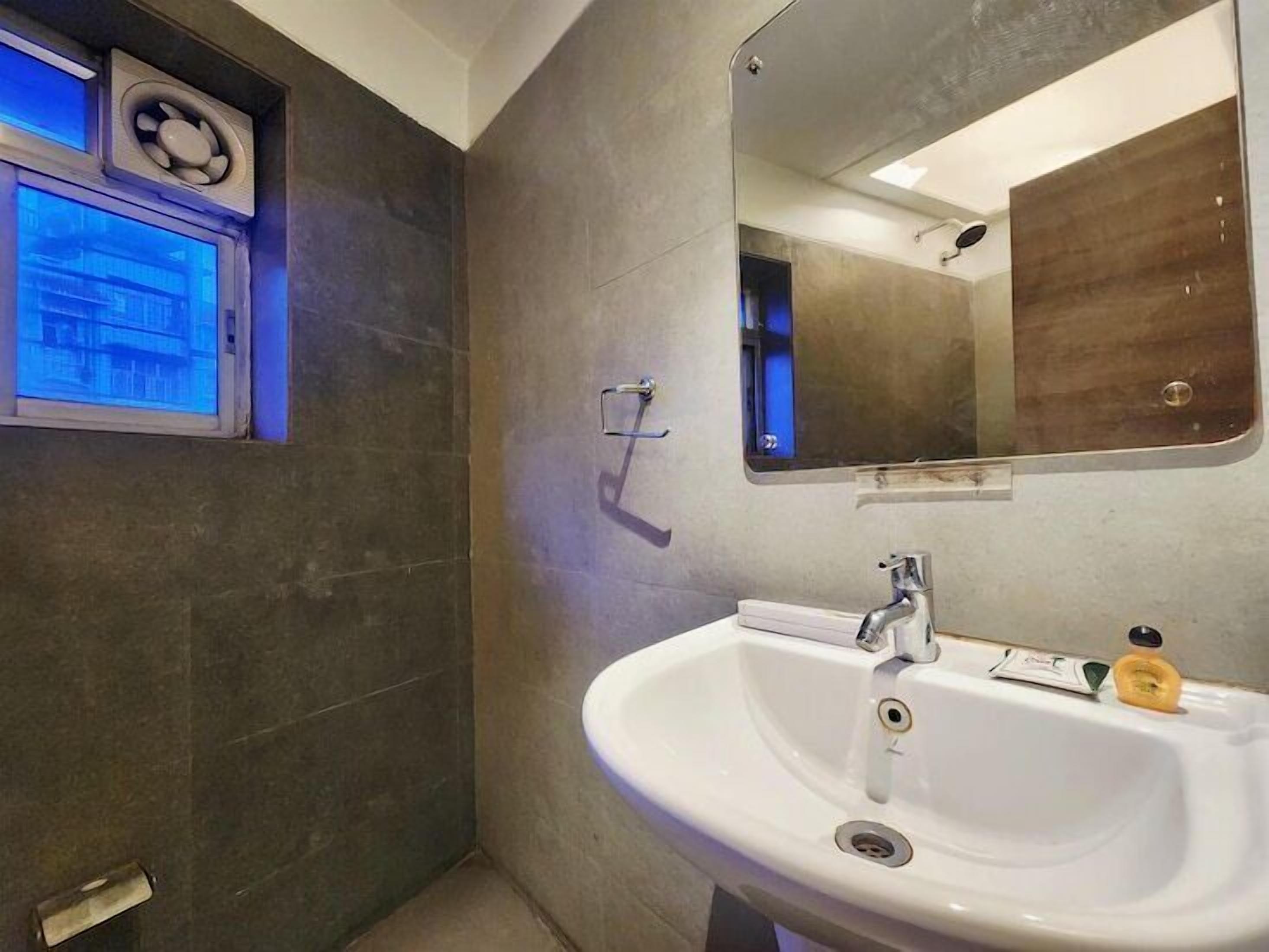 A bathroom with a white sink, a mirror, and a window with a view of buildings.