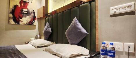 Una habitación de hotel con una cama, una mesita de noche con un teléfono y botellas de agua, y un cuadro en la pared.