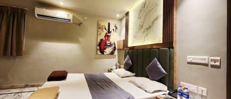 A hotel room with a bed, bedside table, and a wall-mounted air conditioner.