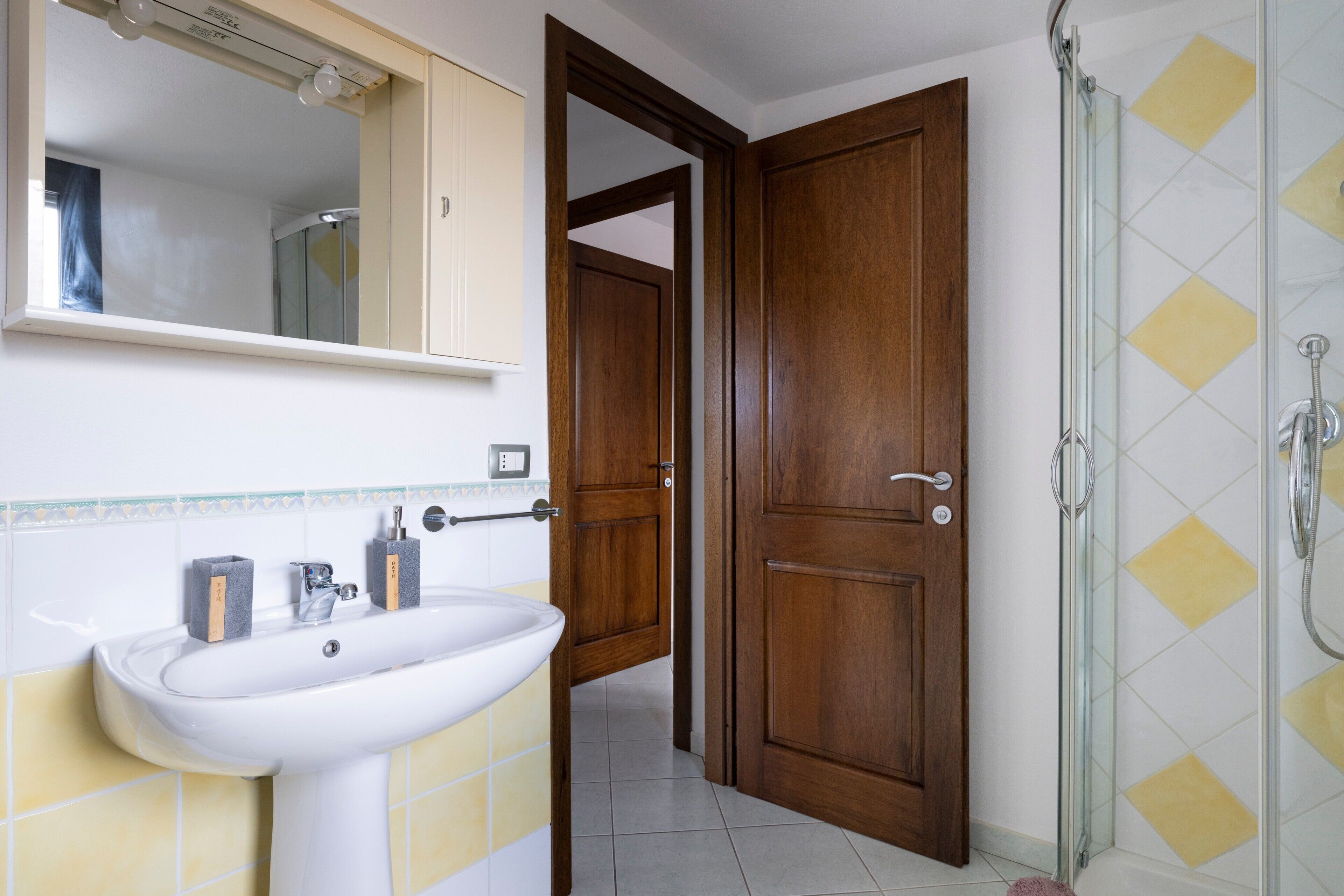 Ein Badezimmer mit Waschbecken, Spiegel, Dusche und Holztür.