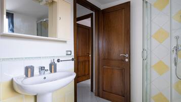 Ein Badezimmer mit Waschbecken, Spiegel, Dusche und Holztür.