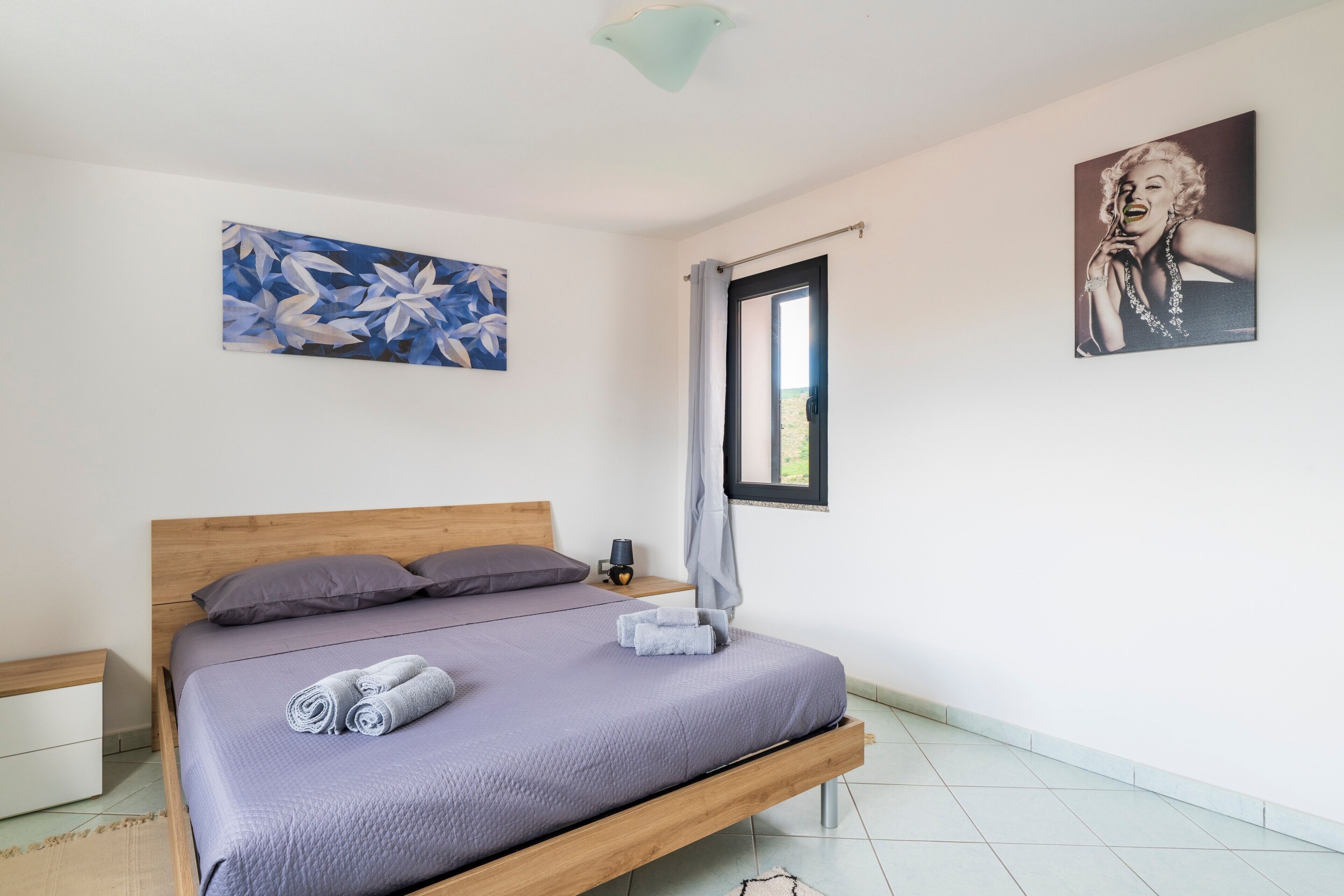 Une chambre à coucher avec un lit, une table de chevet, un tableau, une fenêtre et une porte.