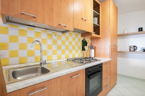 A kitchen with wooden cabinets, a stainless steel sink, a gas stove, and a black oven. - Holiday Home 'Cuccureddu 2' with Sea View, Wi-Fi and Air Conditioning (Jerzu)