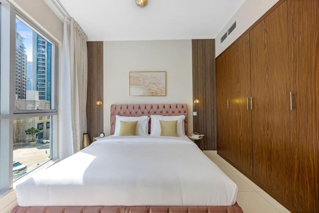 Habitación de hotel con una cama grande, armario de madera y ventana con vistas a la ciudad.
