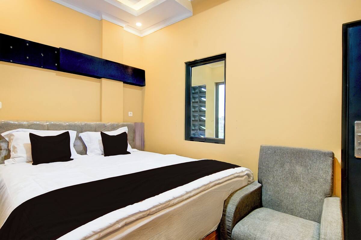 Una habitación de hotel con cama, una silla, una ventana y un estante en la pared.