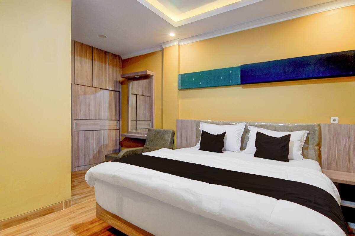 Una habitación de hotel moderna con una cama grande, suelo de madera, un armario empotrado y una obra de arte contemporánea en la pared.