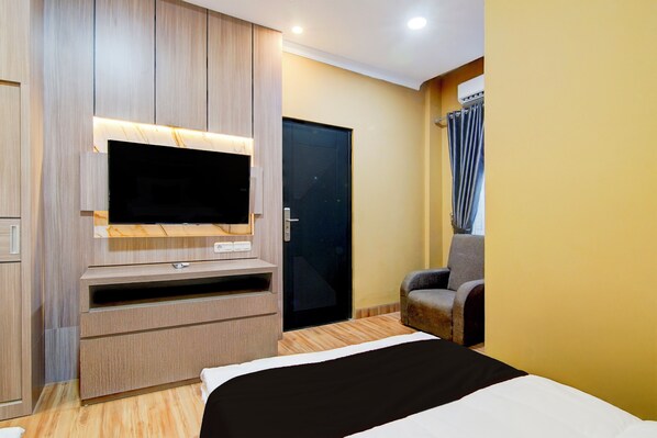 A modern hotel room with a large flat-screen TV mounted on a wooden cabinet, a comfortable armchair, and a closed door.