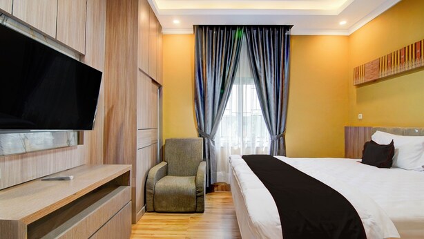 A hotel room with a bed, a TV mounted on a wooden cabinet, a chair, and a window with curtains. - Collection O 94762 Starlight  (Pekanbaru)