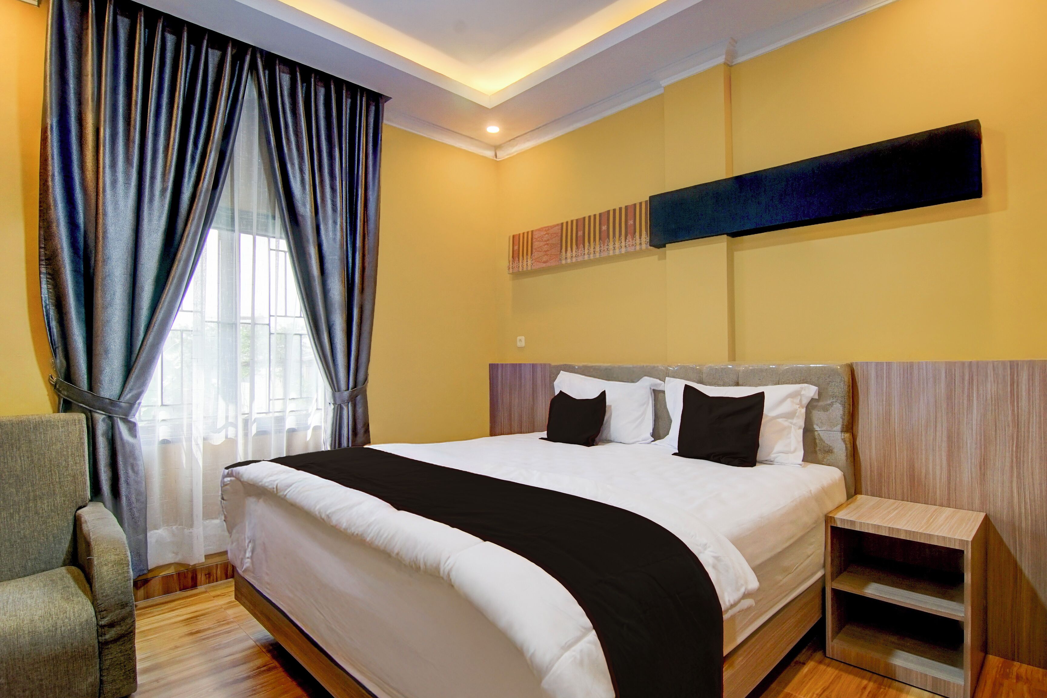 Une chambre d’hôtel avec un grand lit, une chaise, une table de chevet et une fenêtre avec des rideaux.