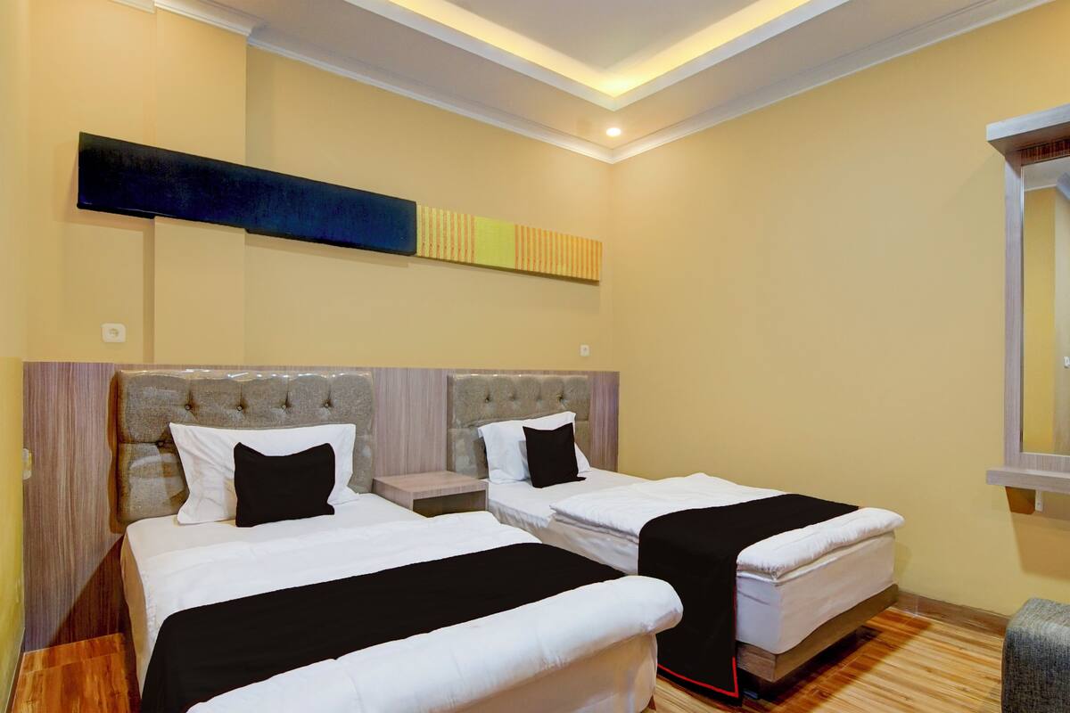 Habitación de hotel con dos camas, cabecero, mesita de noche y espejo.