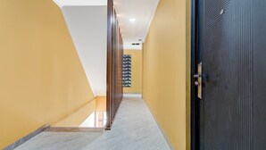 A hallway with a marble floor, a black door on the right, and a yellow wall on the left. - Collection O 94762 Starlight  (Pekanbaru)