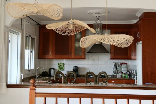 A kitchen with wooden cabinets, a stainless steel range hood, and three woven pendant lights. - Villa Dream View, private pool & spectacular views of the Mediterranean (Lloret Blau)